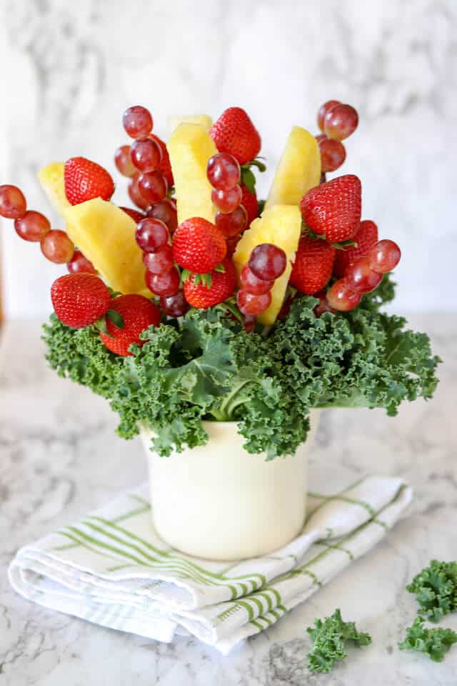 completed fruit arrangement with white vase, kale, grapes, strawberries and pineapple