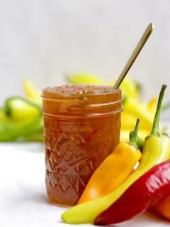 single jar of hot pepper jelly surrounded by peppers