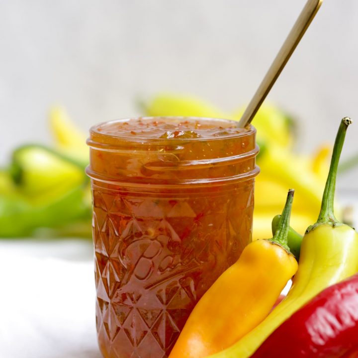single jar of hot pepper jelly surrounded by peppers