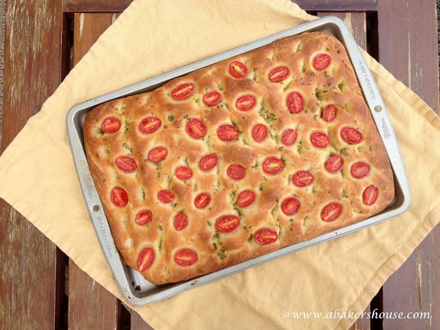 Overhead photo of cherry tomato focaccia on a baking sheet and yellow napkin