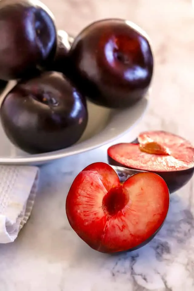 Plum cut in half with bowl of plums in background