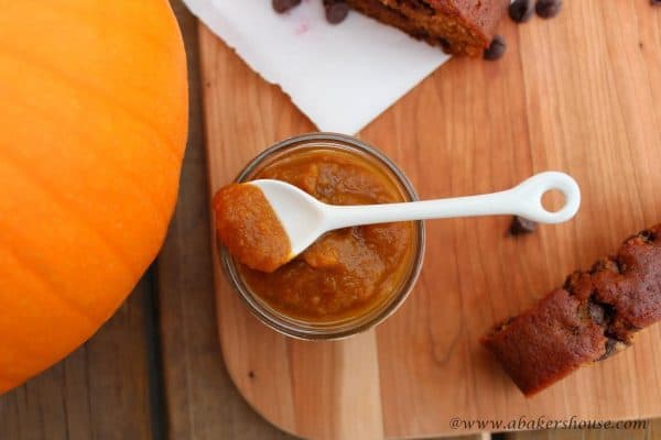 overhead photo of pumpkin butter in a jar on cutting board next to a pumpkin