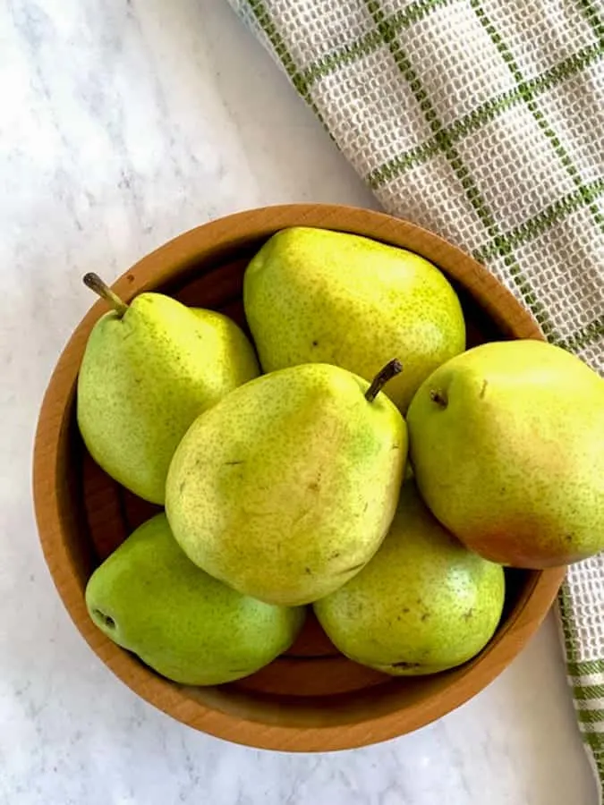 Pears in a wooden bowl on marble countertop