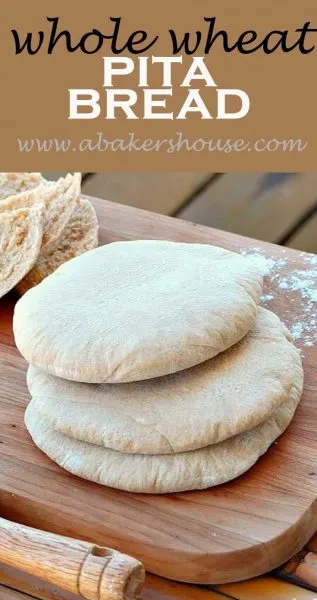 Three Whole wheat pitas on wood cutting board with flour scattered