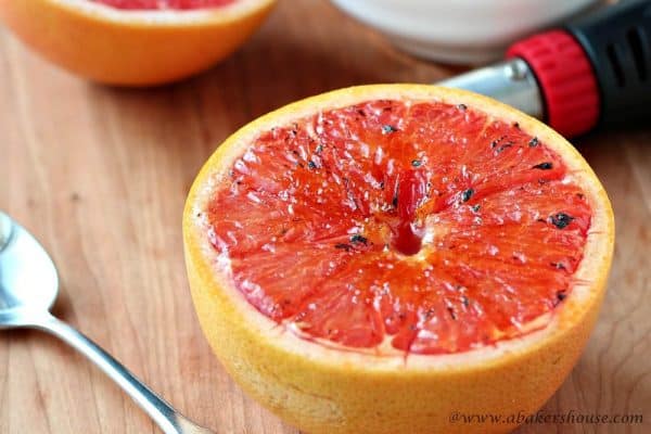 Bruleed grapefruit on a wood board with brulee torch in background