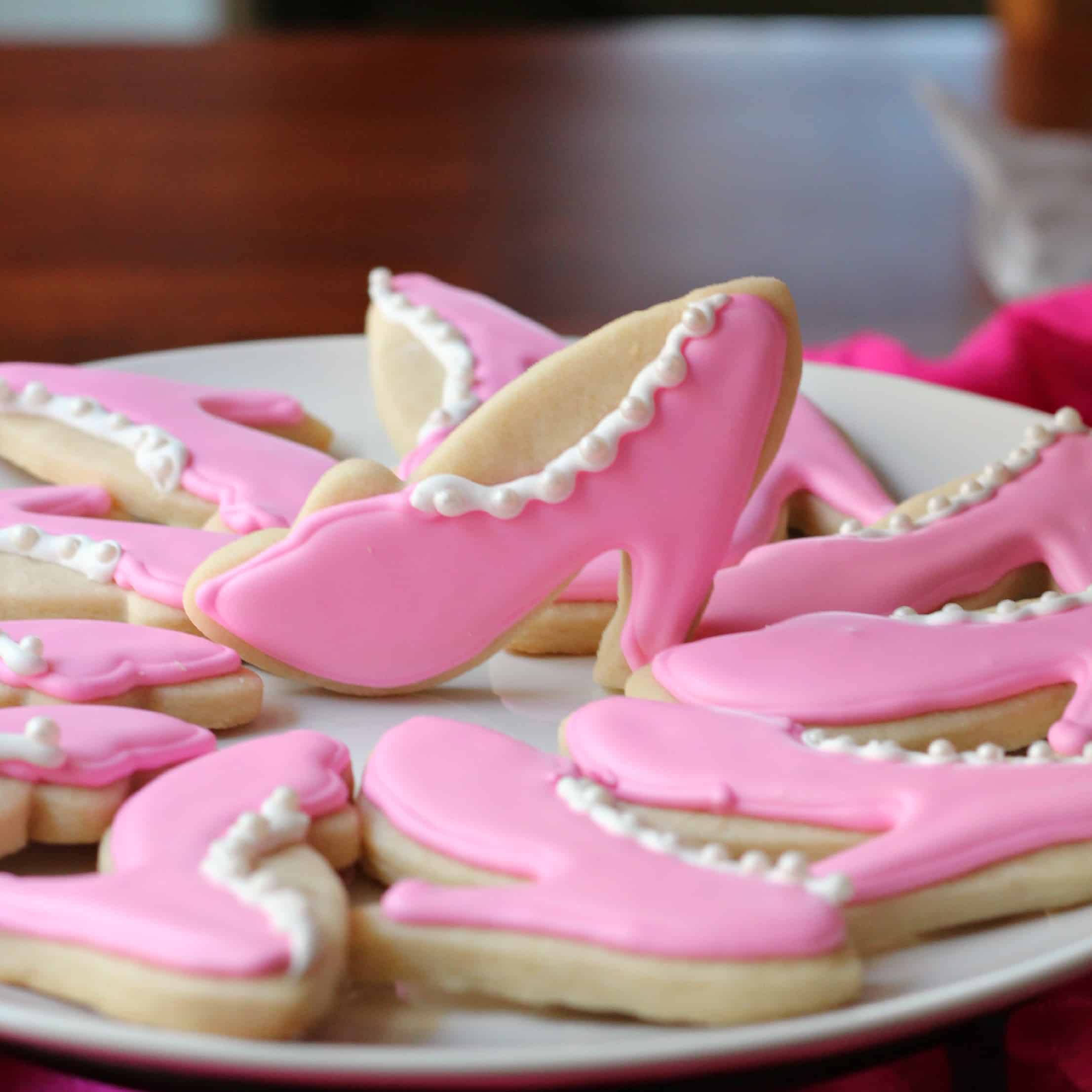 plate full of decorated sugar cookies with royal icing in the shape of high heeled shoes