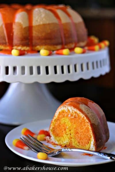 Slice of candy corn Bundt cake with cake on white cake stand in background
