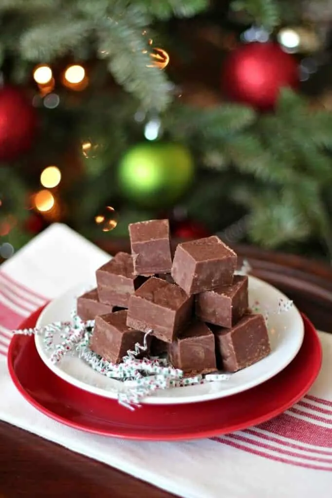 pile of cookie butter fudge on white plate and red plate with Christmas tree in background