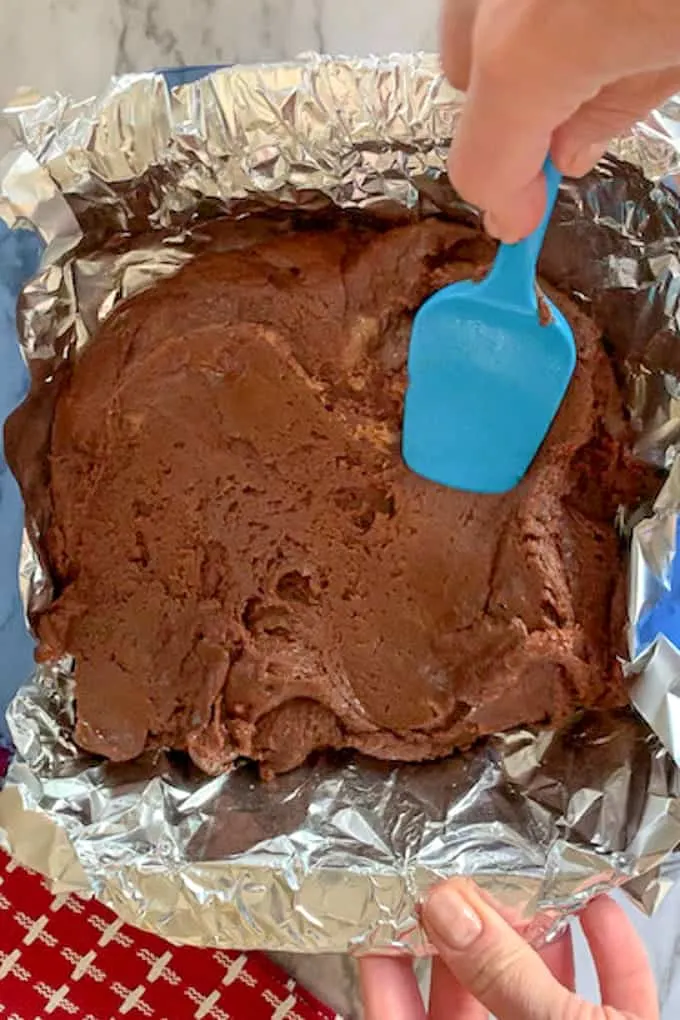 blue spatula spreading the cookie butter fudge in aluminum foil baking pan