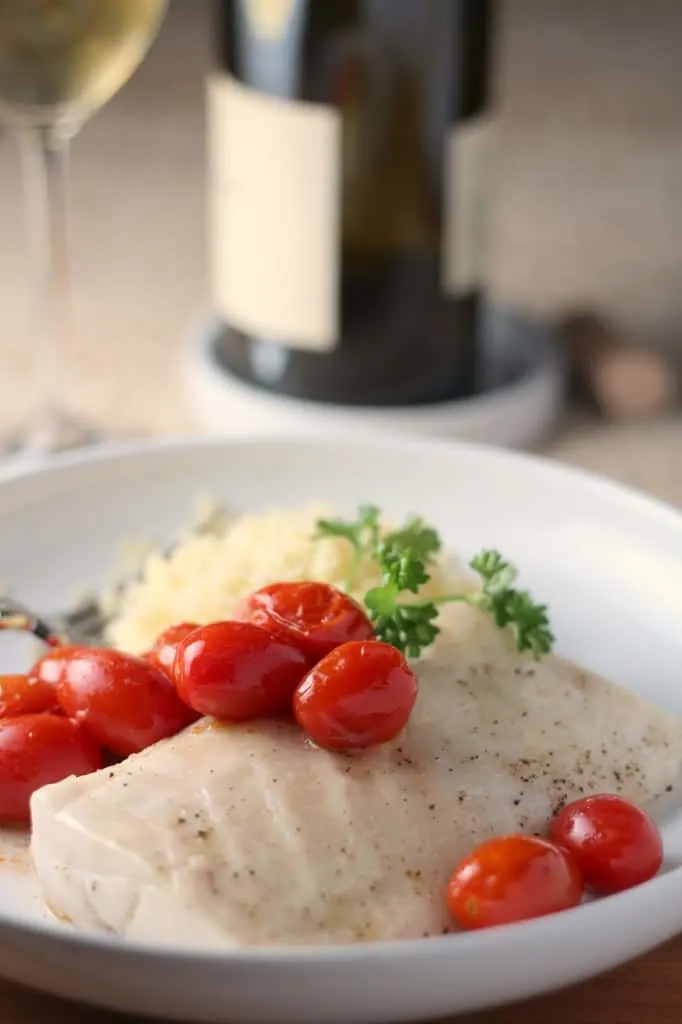 paiche with roasted tomatoes and parsely in a low rimmed white bowl