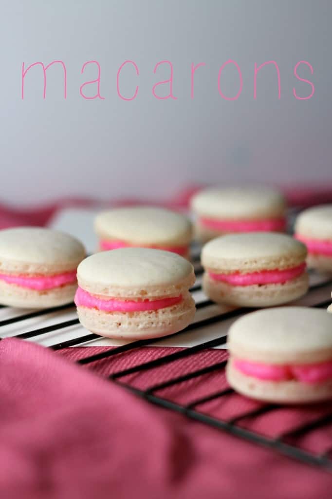macarons with a pink buttercream filling on black wire rack