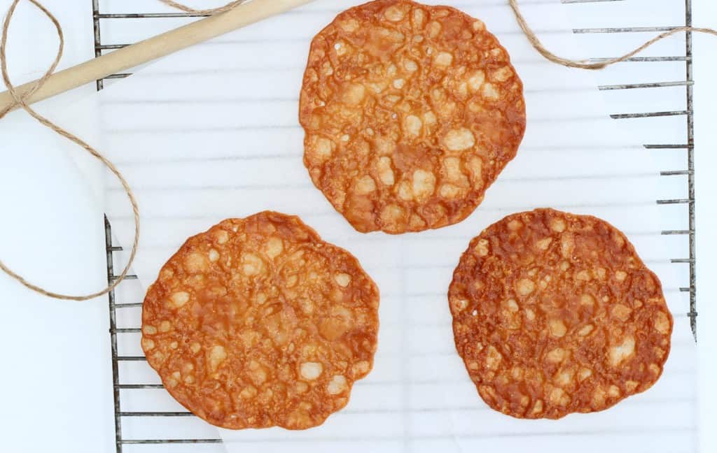 three almond lace cookies on white parchment atop a wire cooling rack