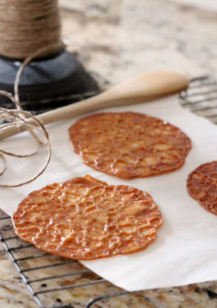 almond lace cookies on white parchment paper with wooden spoon and twine in background