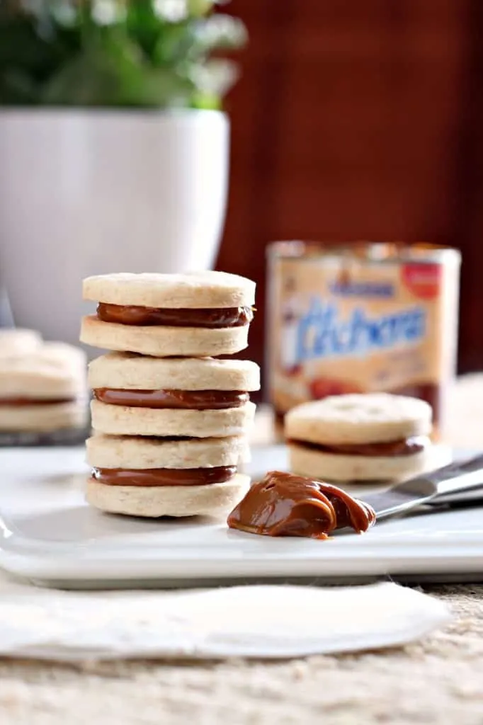 three stacked dulce de leche alfajores sandwich cookies with spoonful of caramel sauce