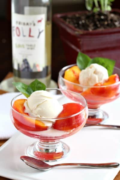 poached peaches with basil in two glass dessert bowls with white wine in background