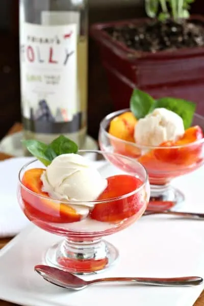 poached peaches with basil in two glass dessert bowls with white wine in background