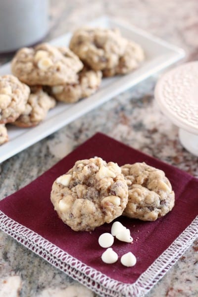 Two Oatmeal white chocolate cookies on dark napkin with a few white chocolate chips