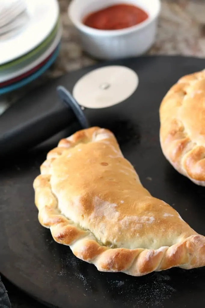 golden brown calzone on black baking stone with pizza cutter