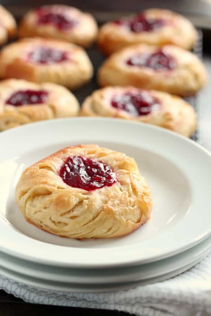 jam filled danish pastry on white plate with baking rack of pastries in background