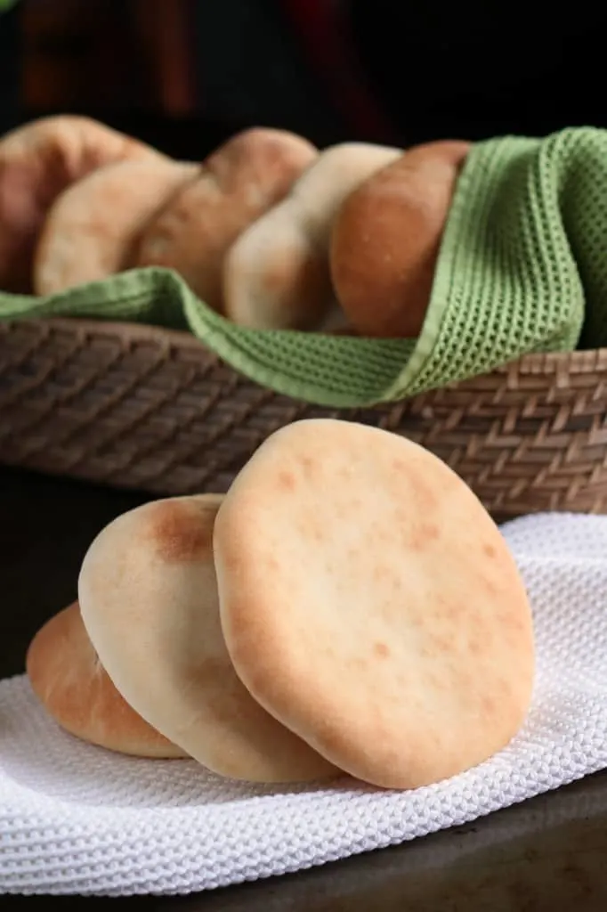 simple pita bread stacked in front of woven basket with green towel