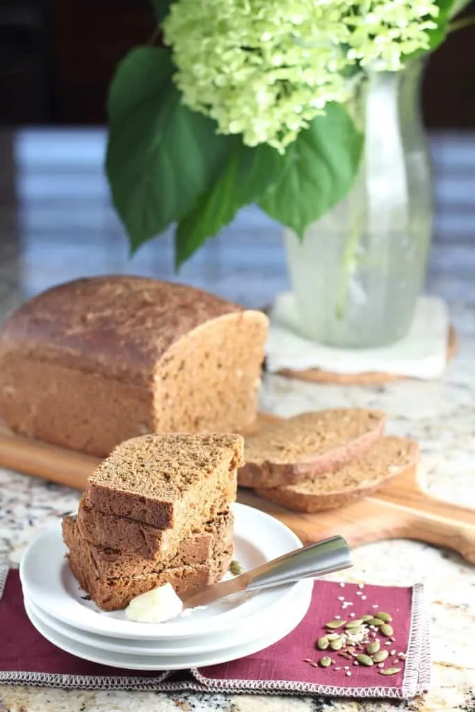 molasses seed bread sliced on a cutting board with flowers in background