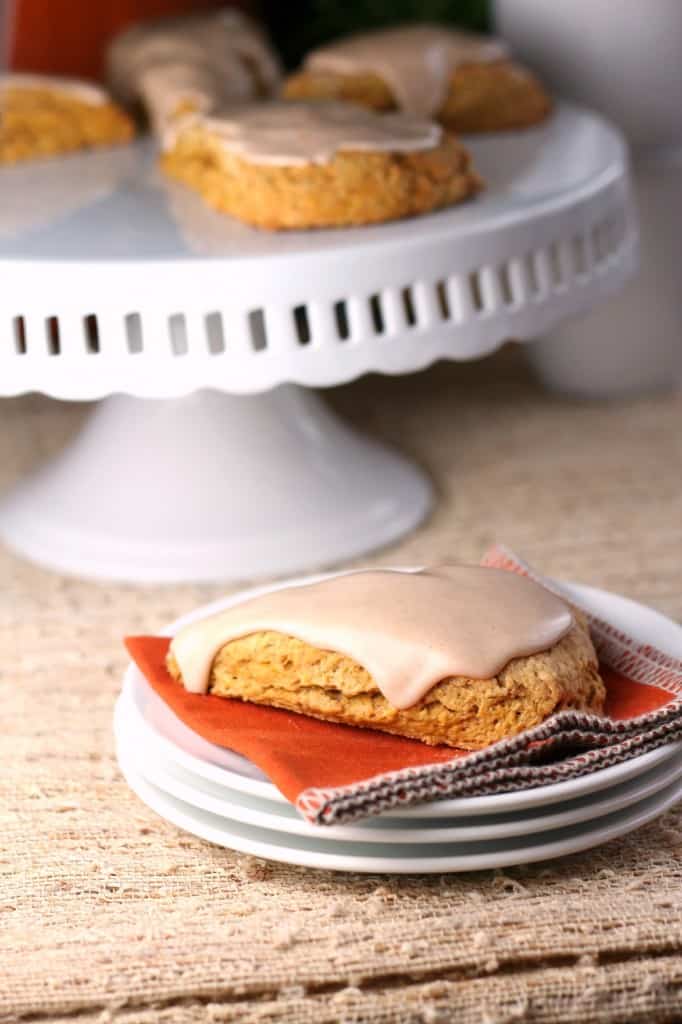 Pumpkin scone with glaze icing on white stack of plates