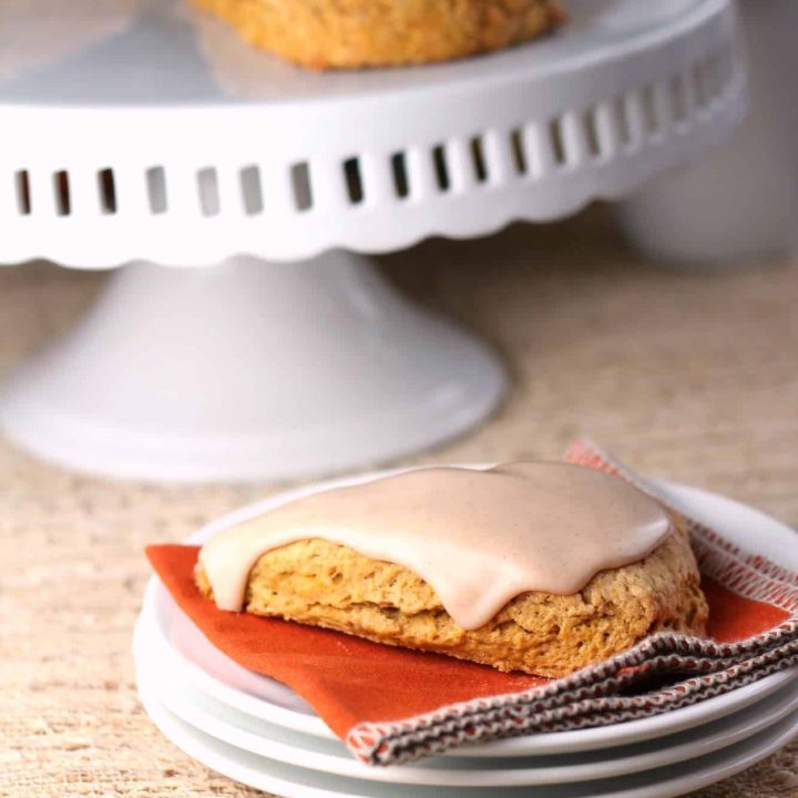 Pumpkin scone with glaze icing on white stack of plates