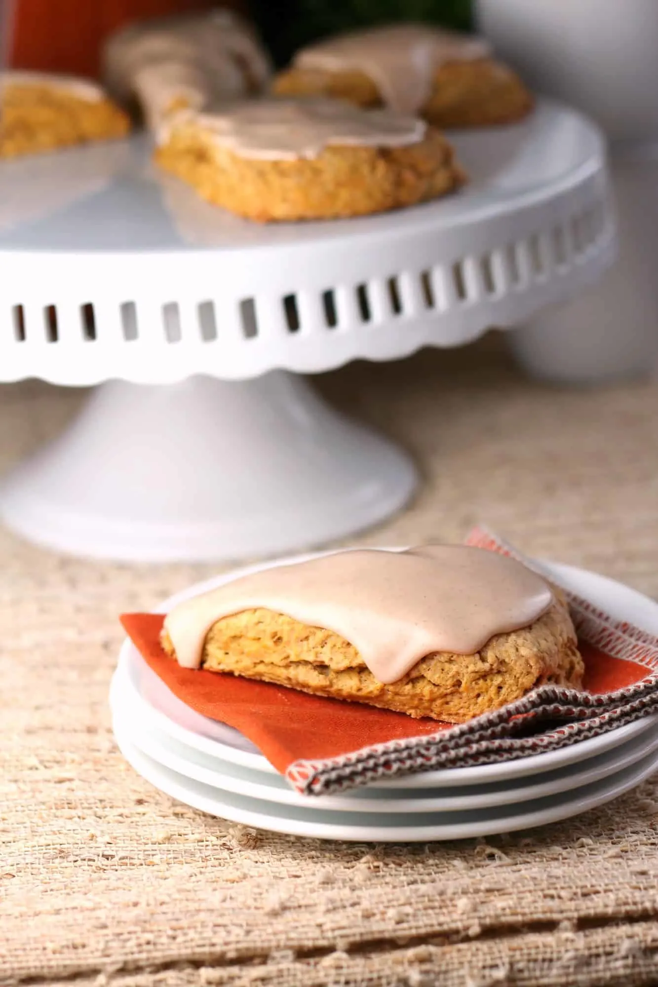 Pumpkin scone with glaze icing on white stack of plates