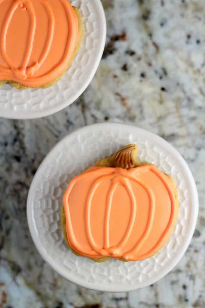 orange iced pumpkin spiced cookies on white plate and granite countertop