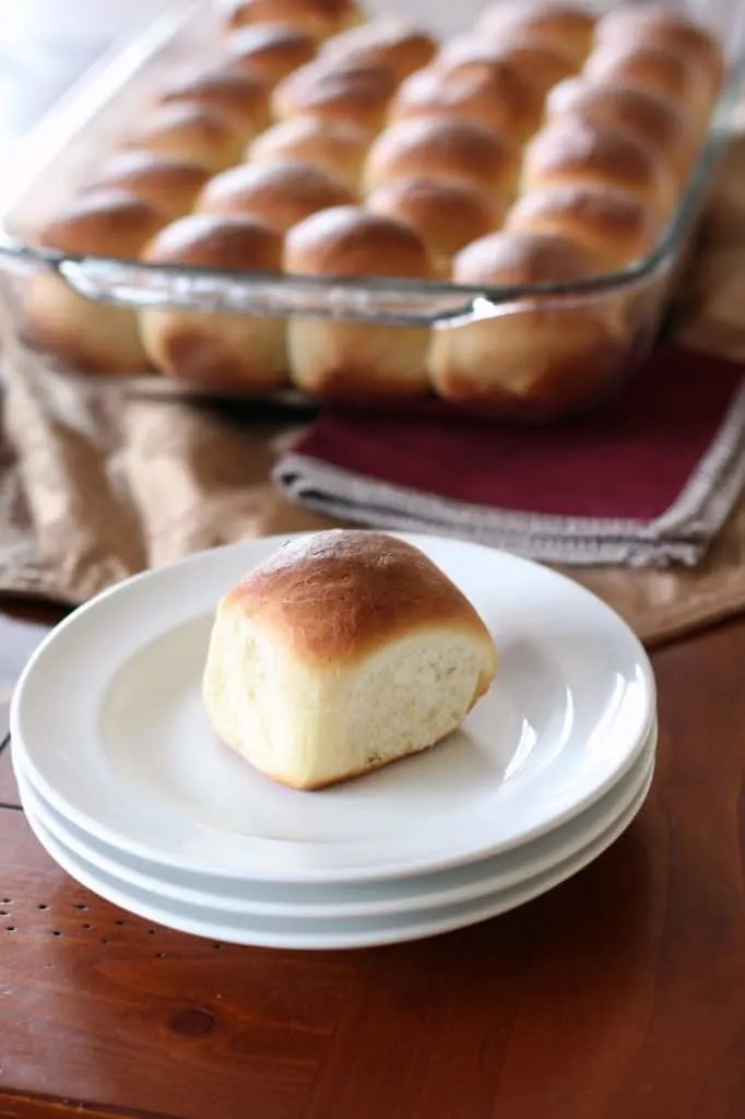 classic dinner roll on white plate with tray of baked rolls in background