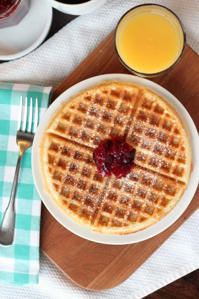 Yeast Belgian Waffle with jam and powdered sugar on white plate with blue checkered napkin