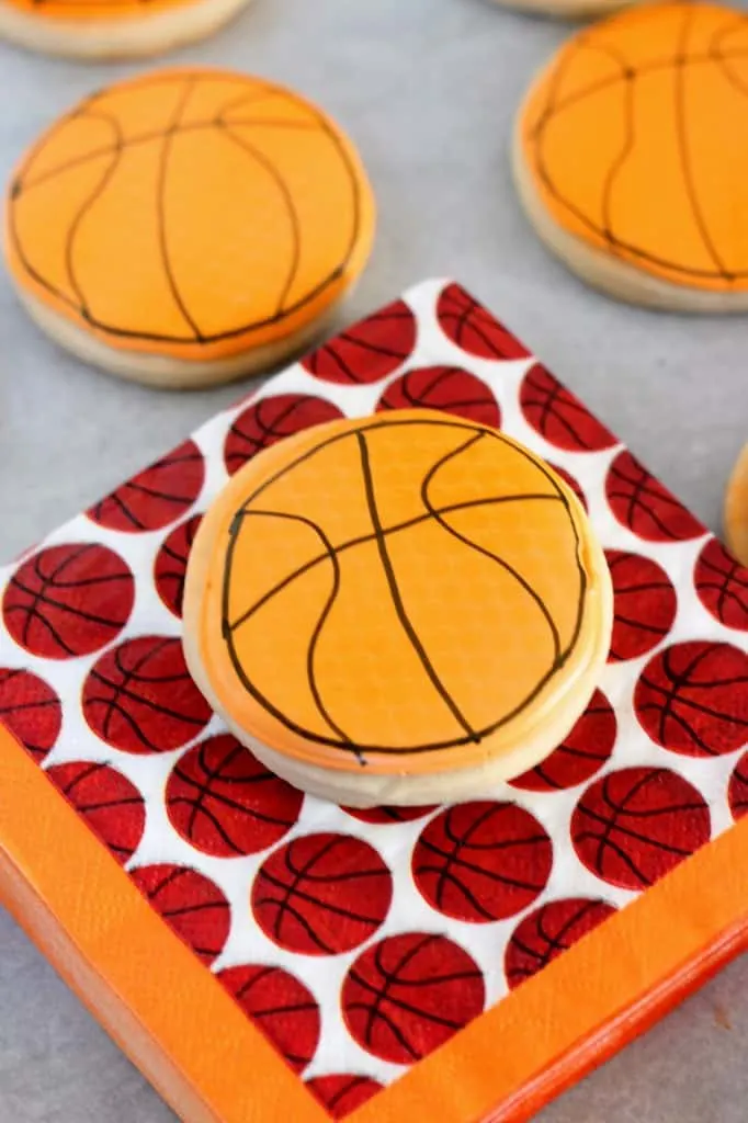 basketball cookie decorated with orange royal icing resting on a basketball napkin