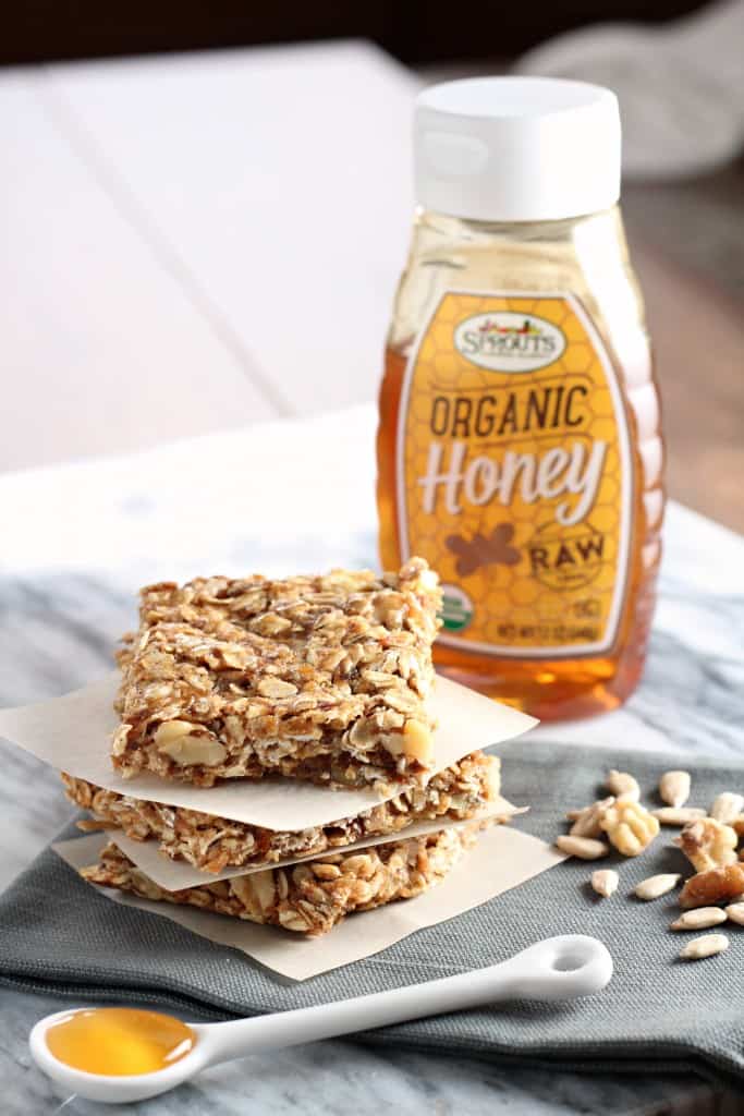 three Honey Oat Granola Bars stacked next to a spoon of honey