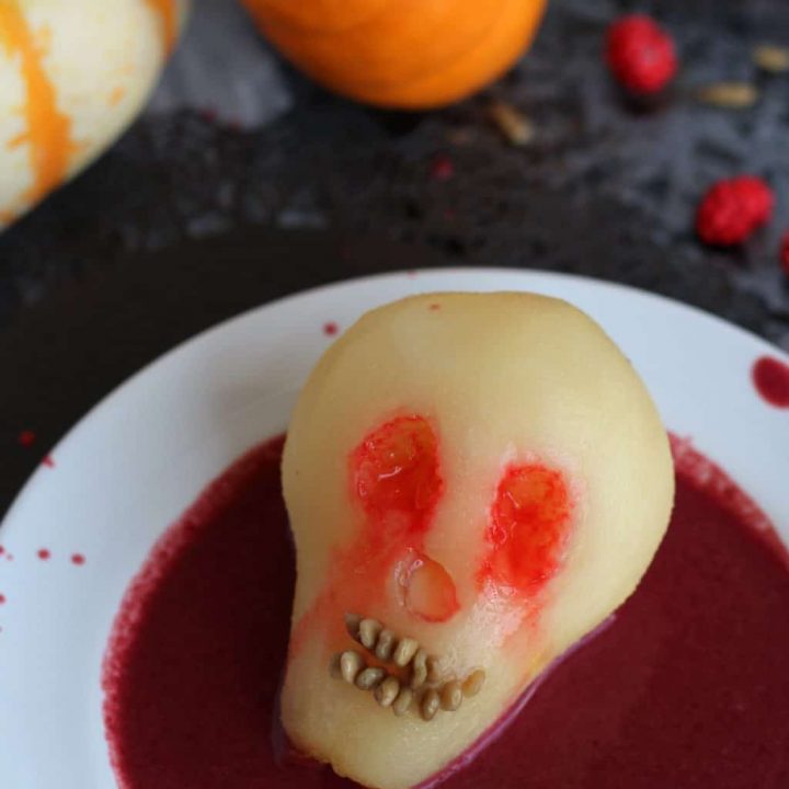 Poached pear for Halloween shaped like a skull in berry sauce