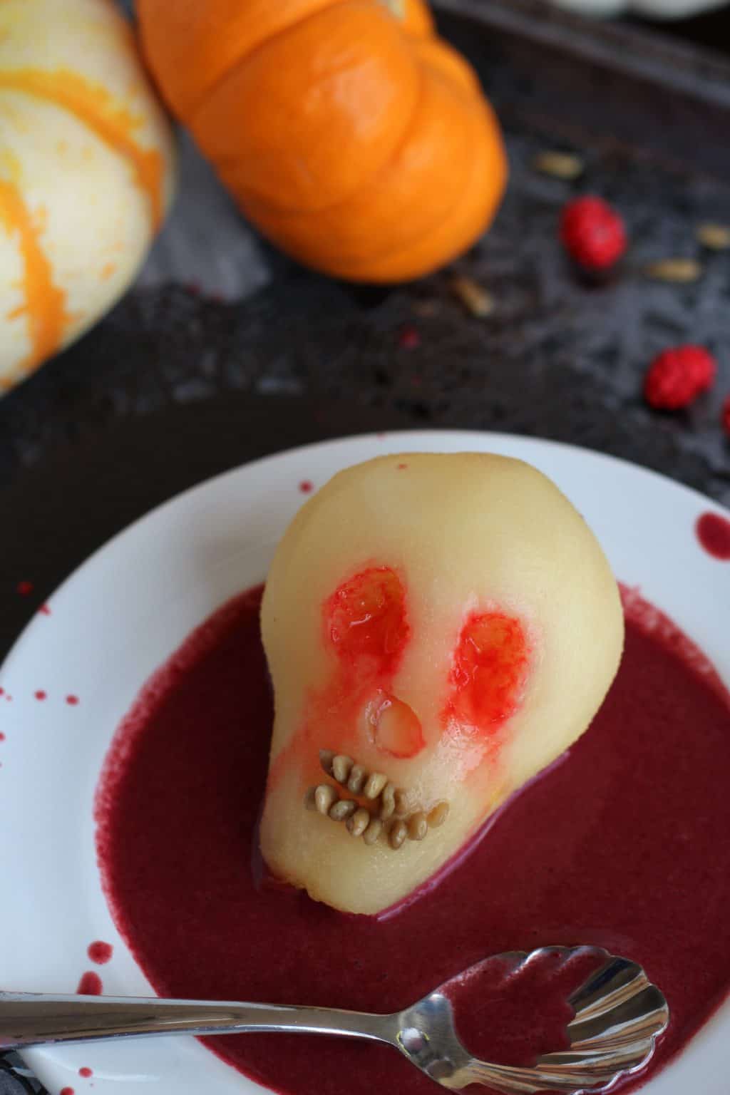 Poached pear for Halloween shaped like a skull in berry sauce