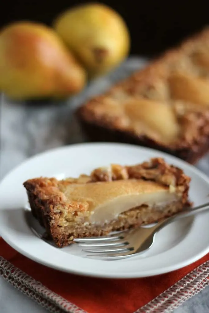 GF pear and walnut tart slice on white plate with pears in background