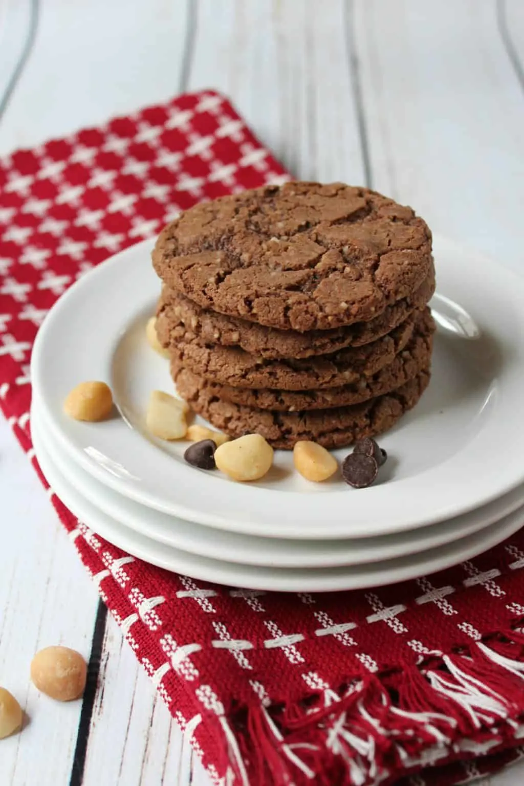 Tall stack of chocolate cookies on white plate with macadamia nuts and chocolate