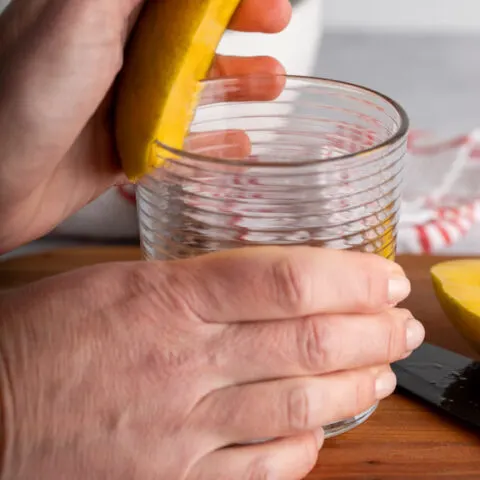 one hand on mango and one on glass to peel mango with glass