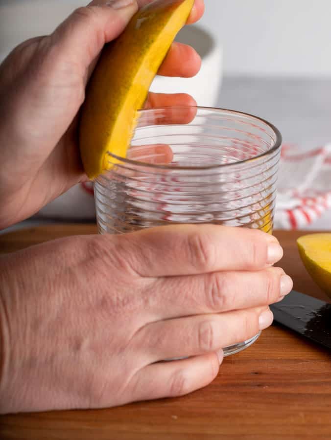 one hand on mango and one on glass to peel mango with glass