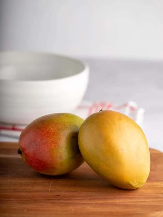 Two mangos on a wooden cutting board