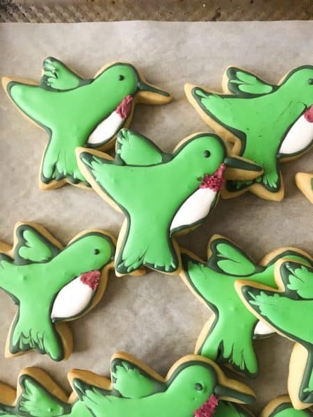 Eight green and white decorated hummingbird cookies on parchment paper