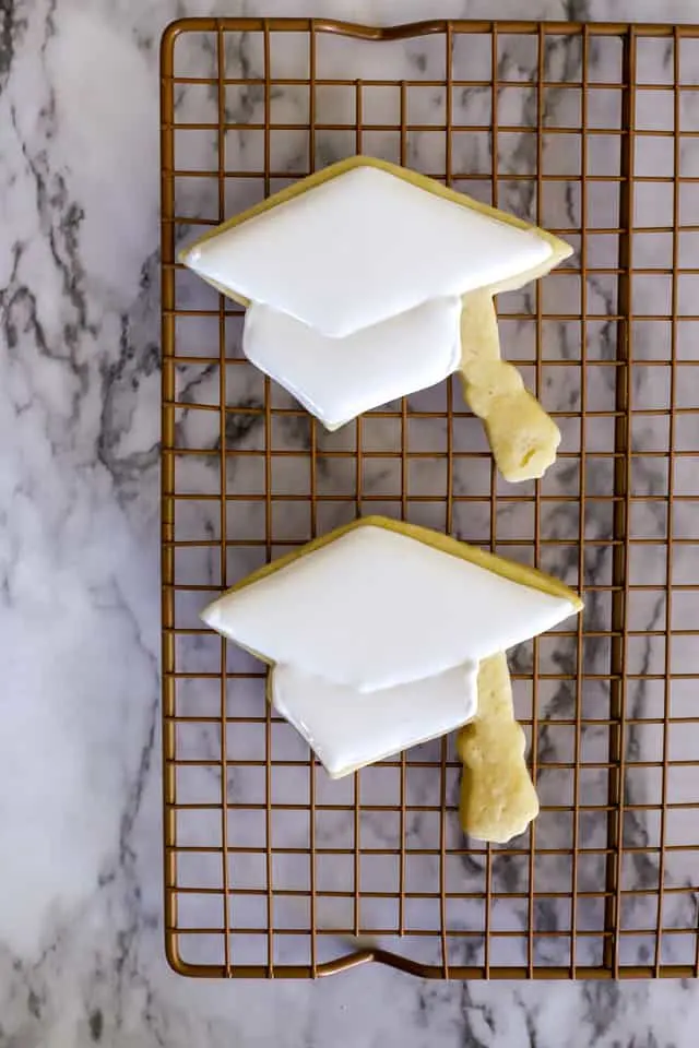 2 cookies shaped like graduation caps with white royal icing