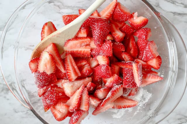 wooden spoon stirring sugar and cut strawberries