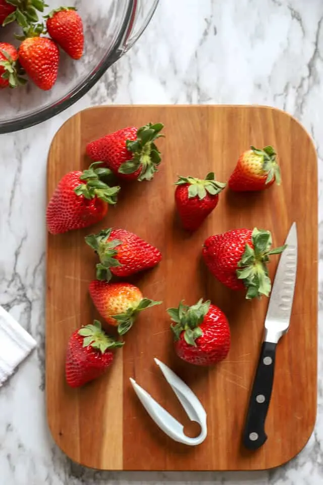 Strawberries ready to be hulled on a wooden cutting board