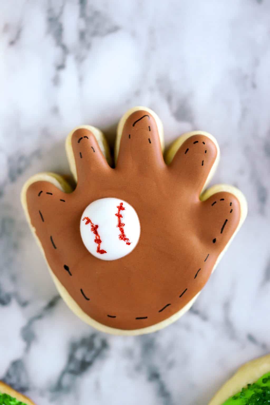 Brown baseball glove cookie with black stitches and a white ball in the glove