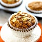 Healthy pumpkin muffin topped with pumpkin seeds or pepitas in a white and aluminum muffin cup on an orange napkin