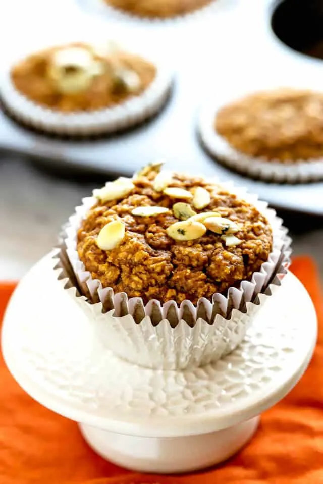 Healthy pumpkin muffin topped with pumpkin seeds or pepitas in a white and aluminum muffin cup on an orange napkin