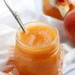 Peach butter in a mason jar with a white napkin and silver spoon