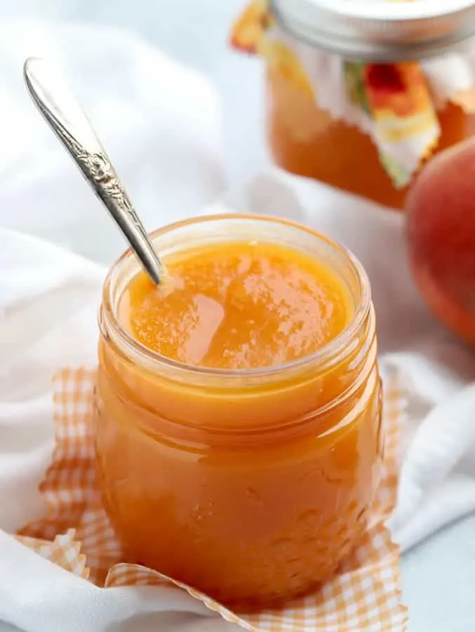 Peach butter in a mason jar with a white napkin and silver spoon