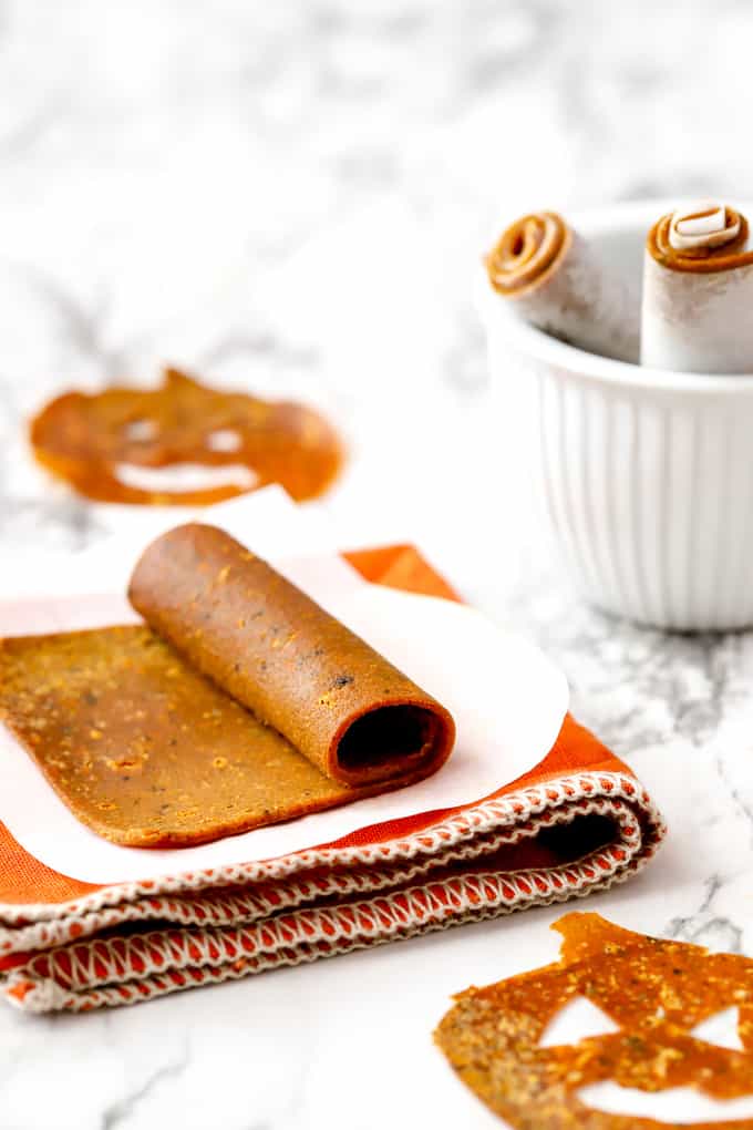 Pumpkin fruit leather roll on parchment with an orange napkin and pumpkin shape in background